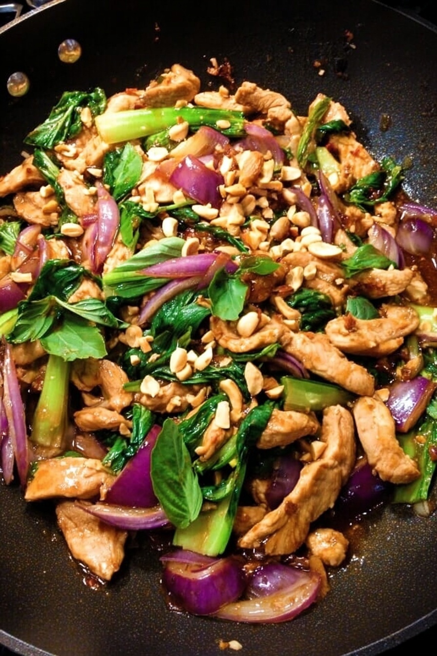 A black wok filled with several layers of stir-fried food: at the bottom are large pieces of bright green bok choy with white stems, and mixed in are soft slices of cooked red onion with a glossy purple color. On top of this layer are medium-sized strips of light brown cooked chicken, slightly shiny from the sauce. Scattered all over are small chunks of beige crushed peanuts adding a rough texture. Fresh green basil leaves are spread on top, adding a pop of leafy color. A wooden spatula appears at the side, resting on the food. The whole dish is on a white marbled surface. Photo taken with an iphone --ar 2:3 --v 7