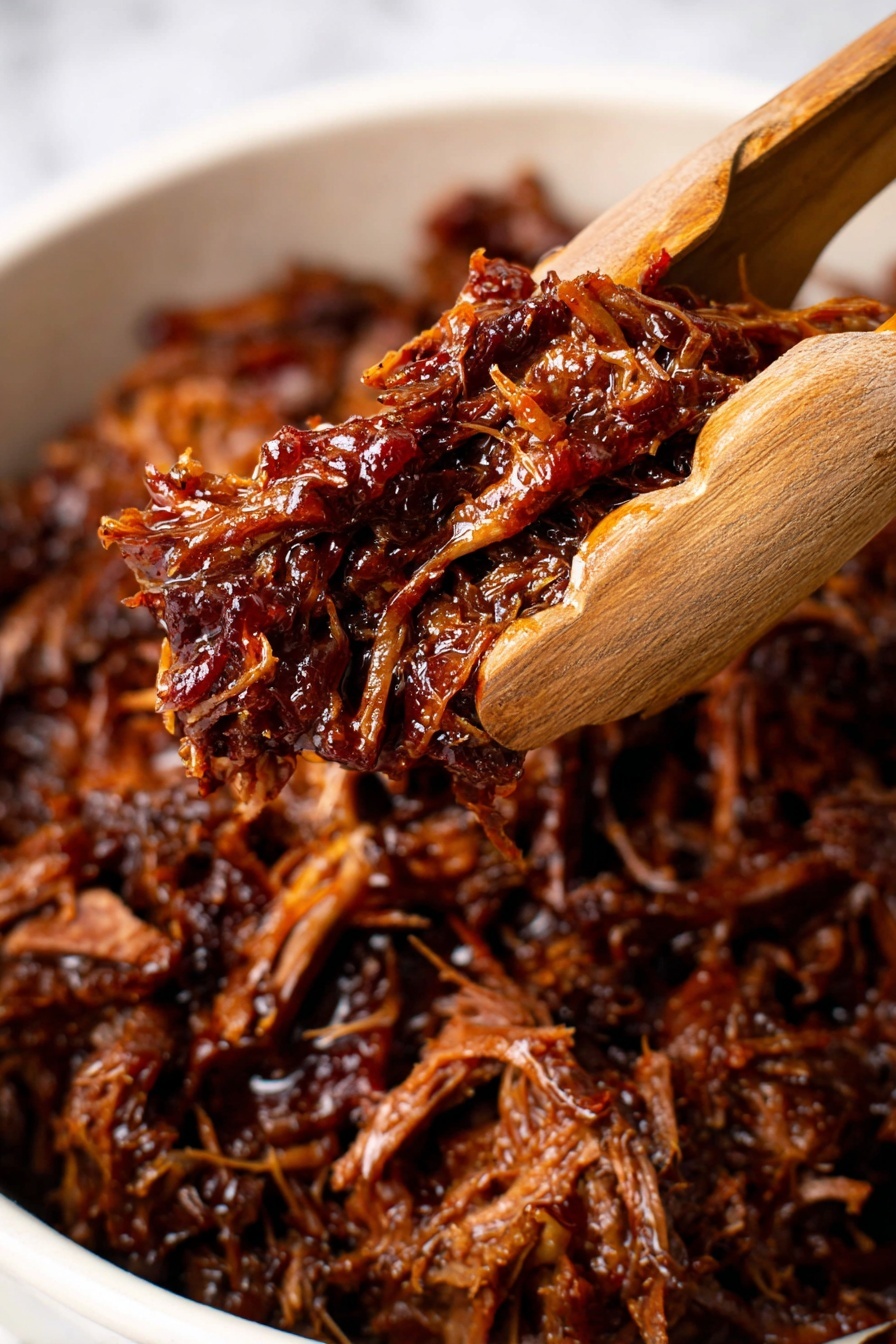 This image shows a close-up of dark brown shredded meat that looks juicy and soft, held by wooden tongs above a white surface with more shredded meat underneath. The meat has a shiny texture from its sauce and appears to have threads and small pieces from slow cooking. The background is blurred, focusing on the meat's rich texture and deep colors. Photo taken with an iphone --ar 2:3 --v 7