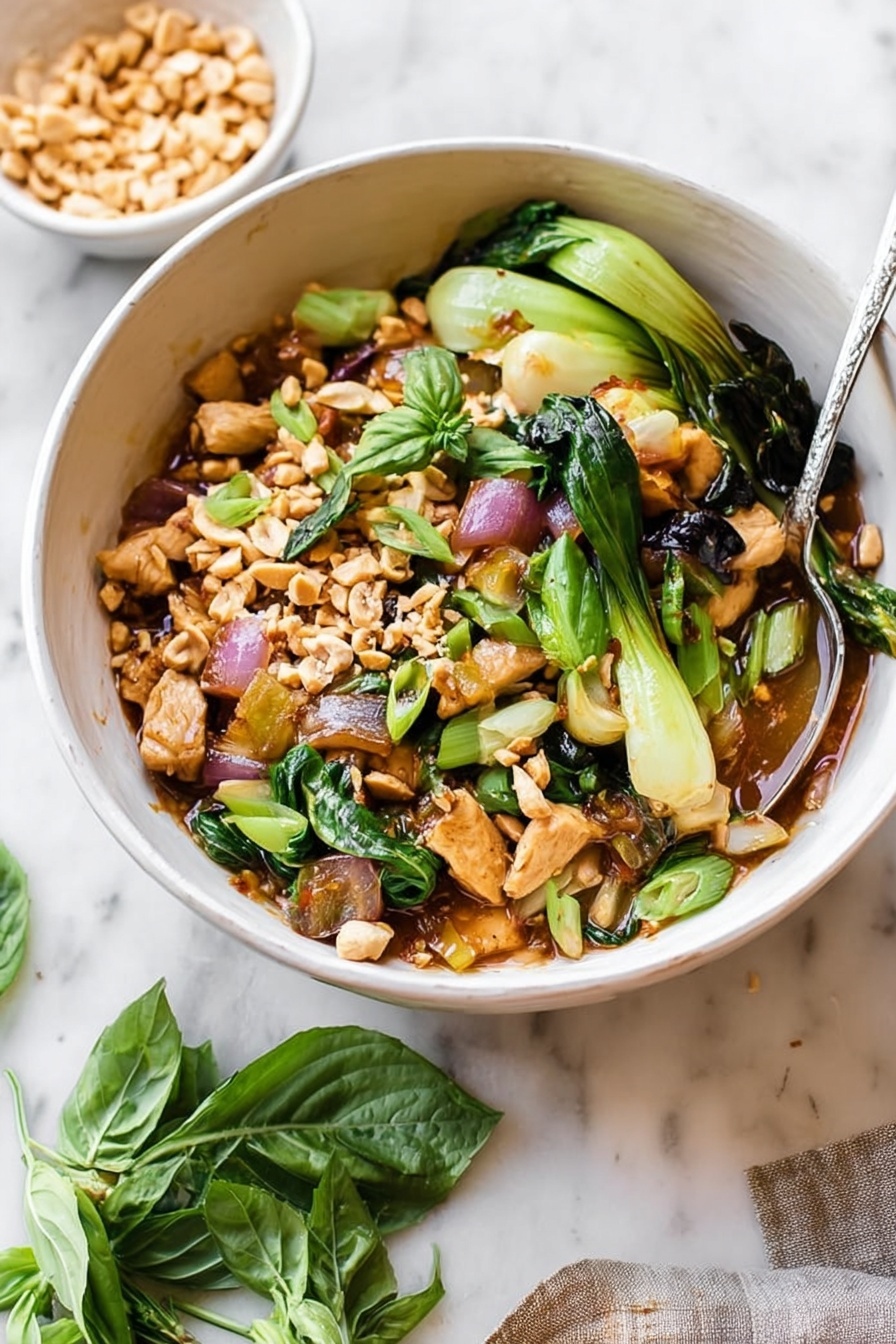 A deep beige bowl filled with a colorful mix of cooked chicken pieces, bright green bok choy, wilted dark green leafy vegetables, and red onion slices in a light brown sauce. The dish is topped with crushed peanuts and fresh green basil leaves, adding texture and freshness. A spoon is placed inside the bowl, and a small white bowl of crushed peanuts sits nearby on a white marbled surface, along with a few loose basil leaves. The lighting is soft and natural, highlighting the vibrant colors and textures of the ingredients. Photo taken with an iphone --ar 2:3 --v 7