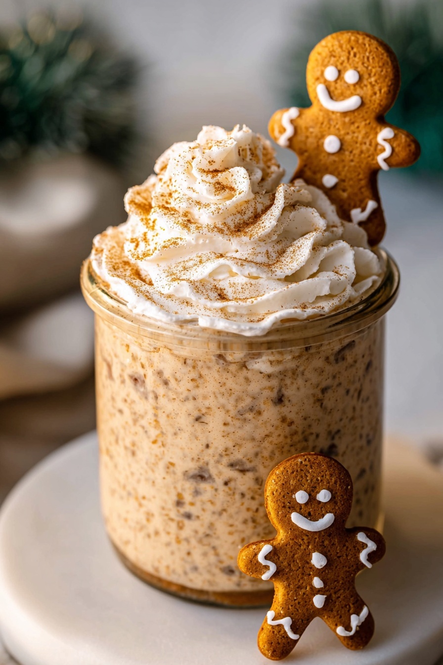 A tall clear glass jar filled with a thick, light brown textured drink mixed with small dark specks. On top, there is a swirl of white whipped cream sprinkled with brown powder, sitting slightly to one side. Next to the whipped cream, a smiling gingerbread cookie decorated with white icing stands upright, its arms raised as if waving. The jar is placed on a plain white plate, all set on a white marbled surface with blurred green miniature Christmas trees in the background. photo taken with an iphone --ar 2:3 --v 7