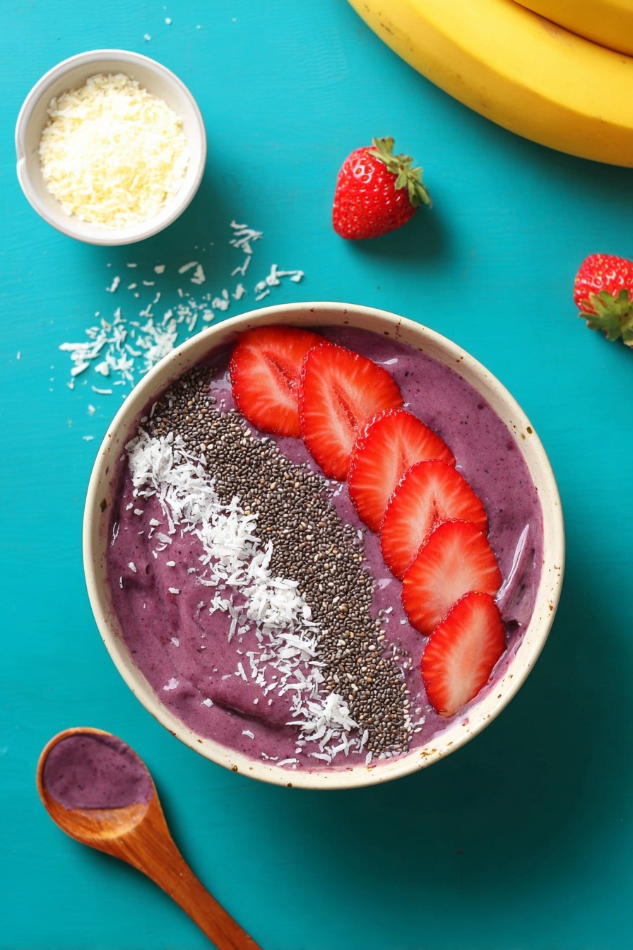 A yellow bowl filled with thick purple smoothie, topped with five bright red strawberry slices on the right side, a line of black chia seeds next to the strawberries, and a curved line of white shredded coconut following the chia seeds along the left side of the bowl's surface. The bowl is on a bright turquoise surface with scattered white coconut flakes around it, a few strawberry slices on the top left, a small brown bowl filled with white shredded coconut on the bottom left, a curved yellow banana at the bottom, and a wooden spoon with a dollop of purple smoothie on the top right. Photo taken with an iphone --ar 2:3 --v 7