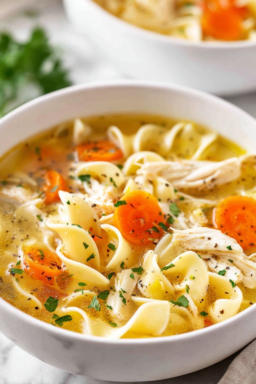 A white bowl full of clear chicken noodle soup held by two woman's hands with glittery pink nail polish. The soup has three layers: the top layer is bright orange carrot slices and pale green celery pieces floating in clear broth, the middle layer shows wide, twisted yellowish egg noodles, and the bottom layer has shredded white chicken bits mixed with chopped green parsley sprinkled on top. The bowl is on a white marbled surface with a spoon nearby. photo taken with an iphone --ar 2:3 --v 7