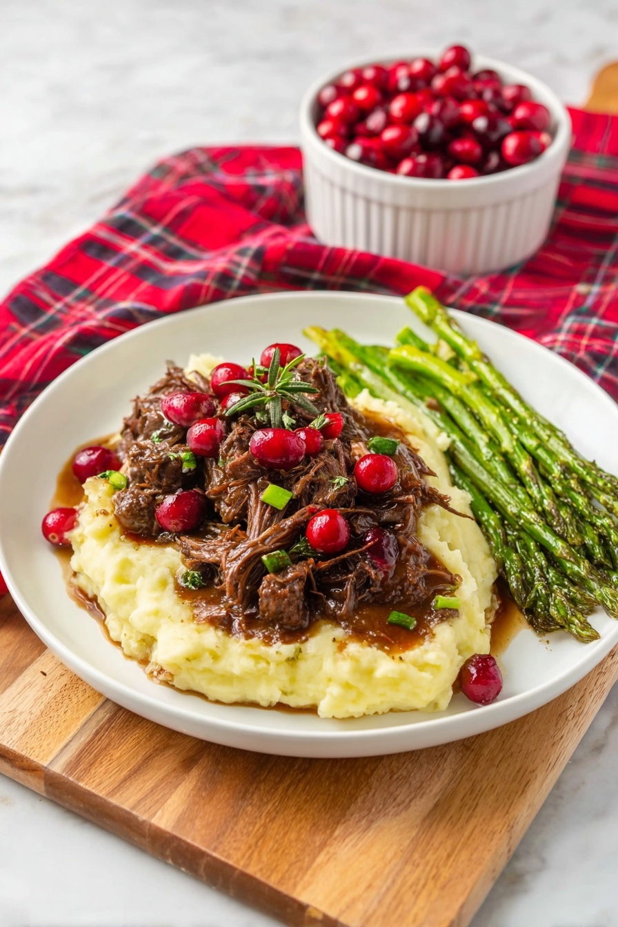 A white round plate shows three main layers of food arranged side by side on a white marbled surface. On the left, a thick white layer of creamy mashed potatoes forms the base. On top of this, there is a pile of shredded brown meat covered in glossy brown sauce and topped with bright red cranberries and a sprinkle of finely chopped green herbs. On the right side of the plate, a neat row of green asparagus spears with a slight shine and light seasoning rests next to the potatoes and meat. Behind the plate, there is a small white cup filled with red cranberries, all set on a red and green plaid cloth draped over a wooden board. Photo taken with an iphone --ar 2:3 --v 7