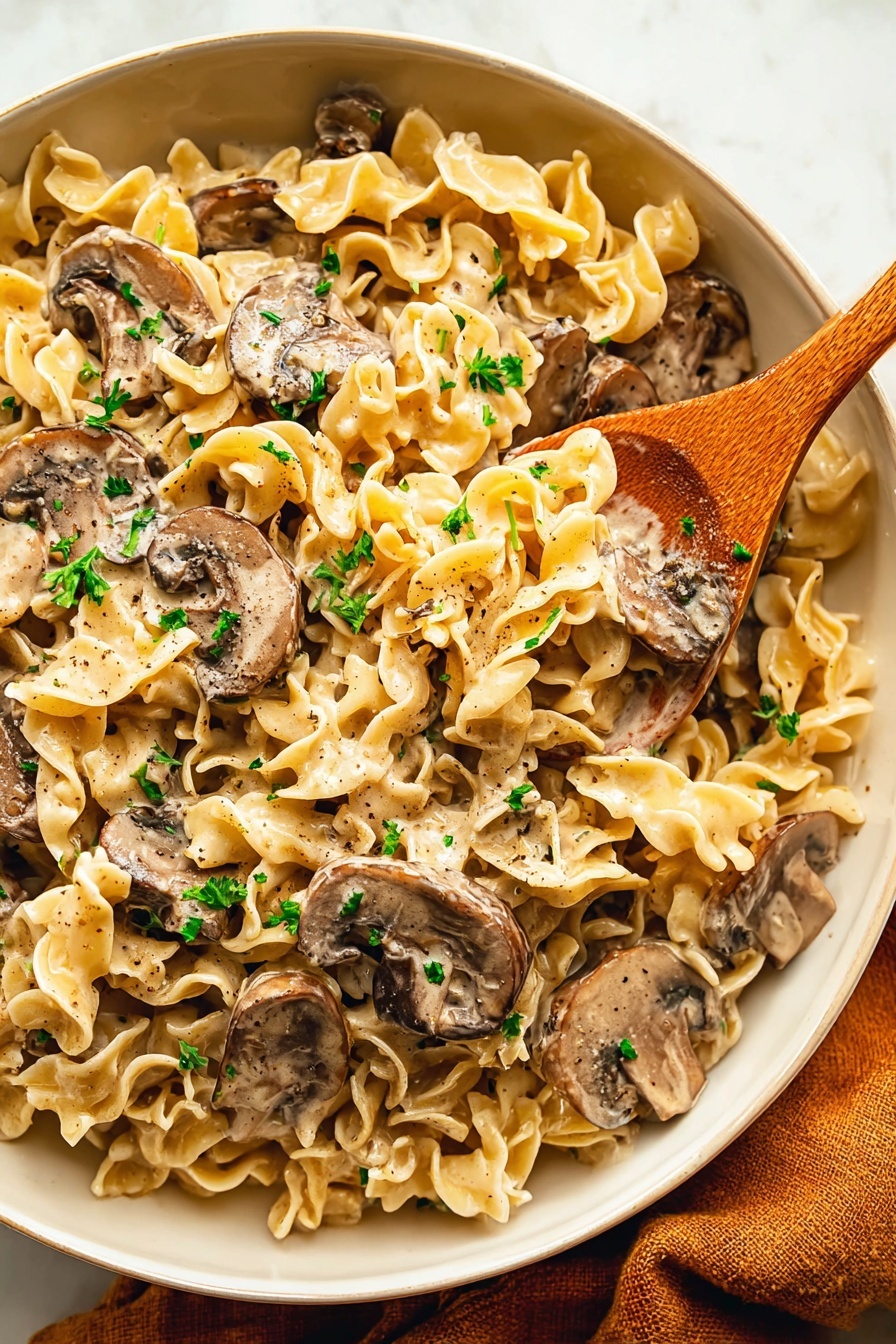 A close-up view of a large white bowl filled with creamy pasta mixed with sliced brown mushrooms, topped with small green parsley pieces. The pasta is light yellow with ruffled edges, covered in a smooth, thick light brown sauce. A wooden spoon is placed inside the bowl on the right side, partially stirring the pasta and mushrooms. The bowl sits on a white marbled surface, with a soft brown cloth partially visible under its edge. Photo taken with an iphone --ar 2:3 --v 7