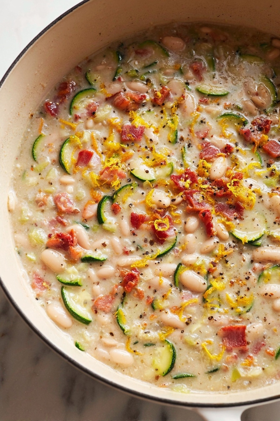 The image shows a close-up of a creamy dish in a white pot on a white marbled surface. The dish has small white beans and round green slices of zucchini mixed throughout. There are small pieces of red bacon scattered over the creamy mixture, which also has visible black pepper and herbs sprinkled on top. The creamy liquid has a smooth texture but is dotted with the solids, giving a mix of colors and textures. Bright yellow zest or small bits add a pop of color among the beans, zucchini, and bacon. Photo taken with an iphone --ar 2:3 --v 7