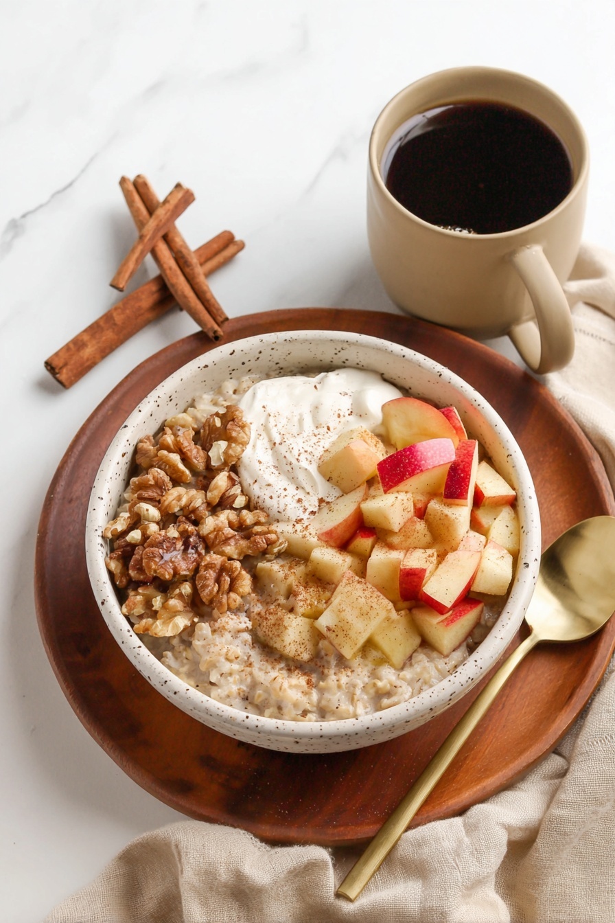 A white speckled bowl filled with a thick layer of light beige oatmeal, topped with three distinct sections: diced cooked apple pieces with red peels, a handful of medium brown walnut halves, and a dollop of white yogurt sitting on top of the walnuts. A golden spoon rests inside the bowl on the oatmeal side. Around the bowl, there are sliced fresh apple pieces on a wooden board, and cinnamon sticks placed on a soft beige cloth, all set on a white marbled surface. photo taken with an iphone --ar 2:3 --v 7