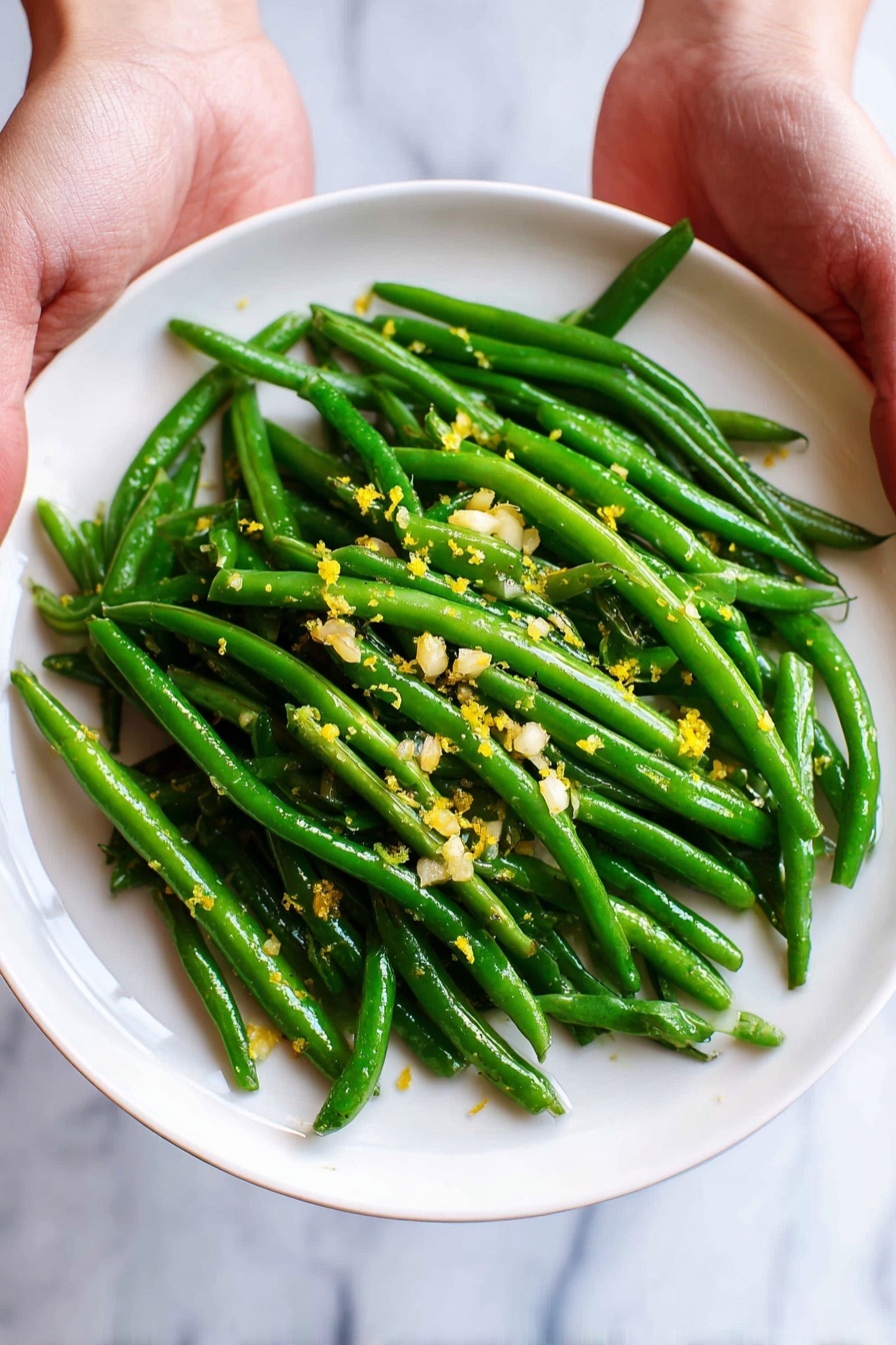 A white plate full of bright green cooked green beans is held by two woman's hands on each side. The green beans look shiny and fresh with small pieces of chopped garlic and tiny yellow lemon zest scattered on top. The plate is set against a white marbled background. photo taken with an iphone --ar 2:3 --v 7