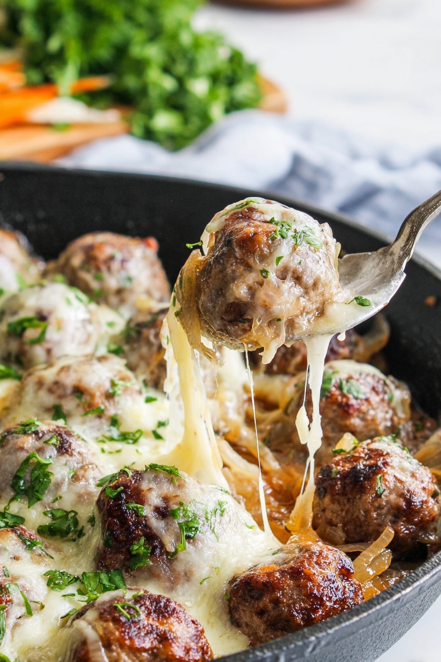 The image shows a black pan filled with browned meatballs on a bed of soft, cooked onions. Each meatball is topped with melted, stretchy white cheese that pulls apart as a spoon lifts one ball. Small green herb pieces are sprinkled over the dish, adding bright color contrast to the warm browns and creamy whites. In the background, there is a blurred bunch of fresh green herbs on a white marbled surface. photo taken with an iphone --ar 2:3 --v 7
