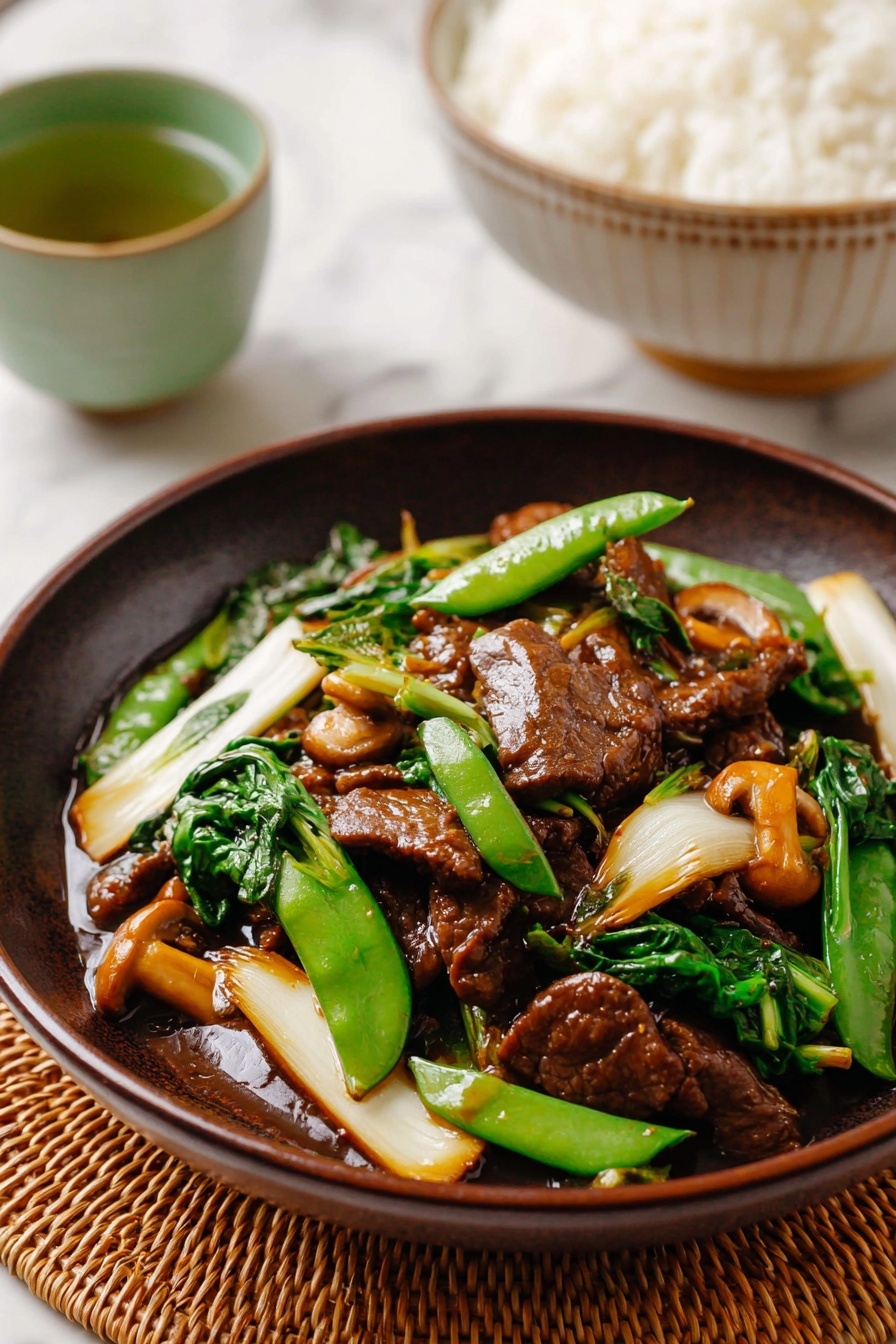 A close-up view of a dark brown bowl filled with a colorful stir-fry dish containing three main layers: at the bottom, a glossy reddish-brown sauce coating tender pieces of seared meat, in the middle, bright green snap peas and fresh leafy greens, and on the top, thick, soft white and light yellow vegetable slices including bok choy and mushrooms, all mixed together. The bowl is placed on a light tan bamboo mat with a pair of wooden chopsticks resting nearby on a white marbled surface. In the blurred background, there is a white bowl with blue patterns filled with white rice, and a small green ceramic cup filled with green tea. Photo taken with an iphone --ar 2:3 --v 7