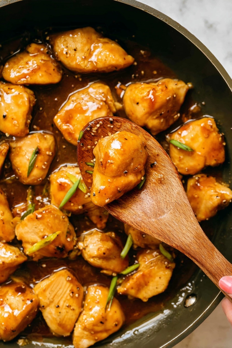 The image shows a wooden spoon holding two shiny, golden brown cooked chicken pieces covered in a glossy sauce with a small green onion slice, above a skillet filled with similar chicken pieces in the same sauce, sprinkled with black pepper and green onion slices. The chicken pieces are plump with a slightly caramelized surface, resting in a rich, glossy amber-colored sauce that pools in the skillet beneath them. The background is a white marbled texture. photo taken with an iphone --ar 2:3 --v 7