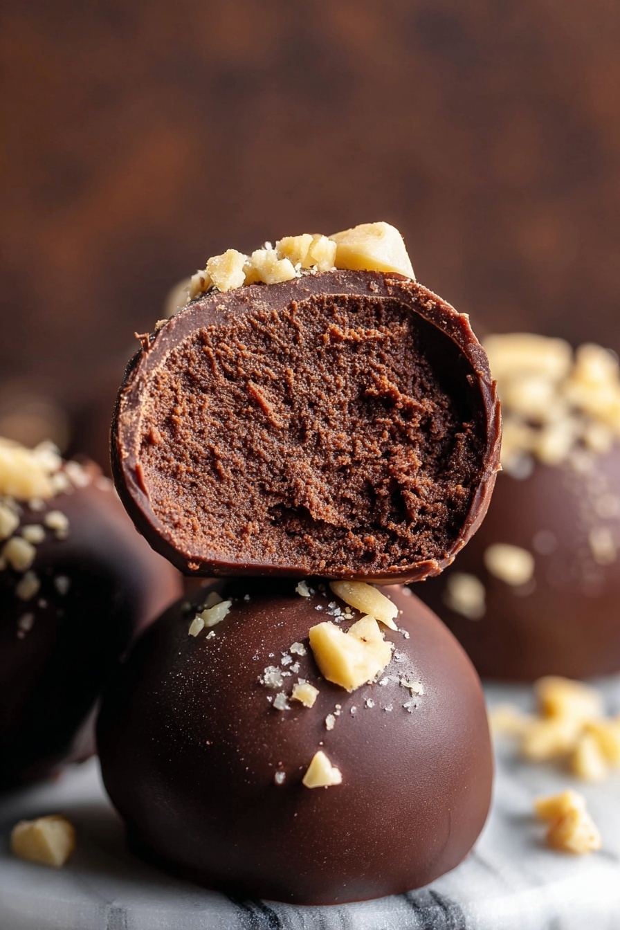 Seven round chocolate balls are placed closely together in a small white bowl, each ball coated with a smooth, dark chocolate layer. The tops of the balls are sprinkled with small pieces of chopped nuts, creating a light tan and slightly rough texture against the dark, shiny chocolate. The bowl sits on a white marbled surface, adding a clean and bright contrast to the rich colors of the chocolate and nuts. photo taken with an iphone --ar 2:3 --v 7