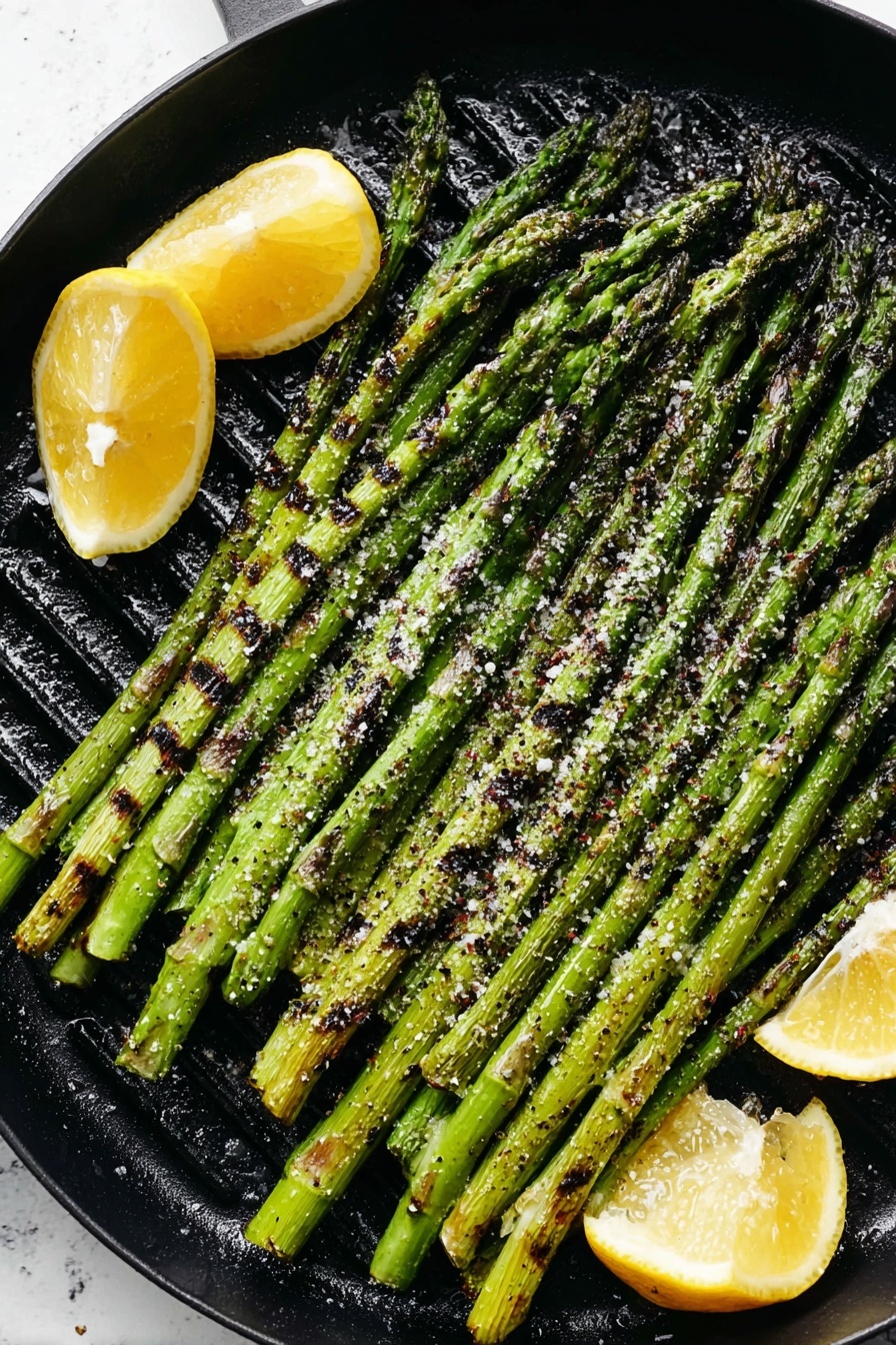 A black grill pan holds one layer of long, green grilled asparagus stalks, placed side by side covering the pan. The asparagus has dark char marks and is sprinkled with coarse salt. Around the edges of the asparagus, there are four bright yellow lemon wedges with black grill spots. The background is a white marbled texture. photo taken with an iphone --ar 2:3 --v 7