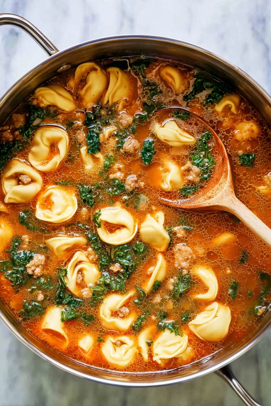 A close-up view of a silver pot with two light gold handles, filled with a bright orange broth containing many small, folded cheese tortellini pieces that are pale yellow with smooth edges. Scattered throughout the soup are chopped kale leaves in dark green, some small chunks of brown meat, and bits of carrot that add a touch of orange. A wooden spoon rests inside the pot, partially submerged in the soup, showing the texture of the broth and ingredients. The pot sits on a white marbled surface. photo taken with an iphone --ar 2:3 --v 7