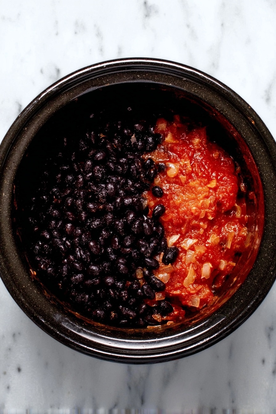 The image shows a black slow cooker on a white marbled surface, filled with two clear layers of food. The bottom layer is a thick, chunky red sauce with small bits of ingredients visible, while the top layer is a dense, shiny black bean mixture, sitting neatly above the red sauce and filling about half of the cooker. The clean separation between the two layers creates a strong contrast between the dark black beans and the bright red sauce. Photo taken with an iphone --ar 2:3 --v 7