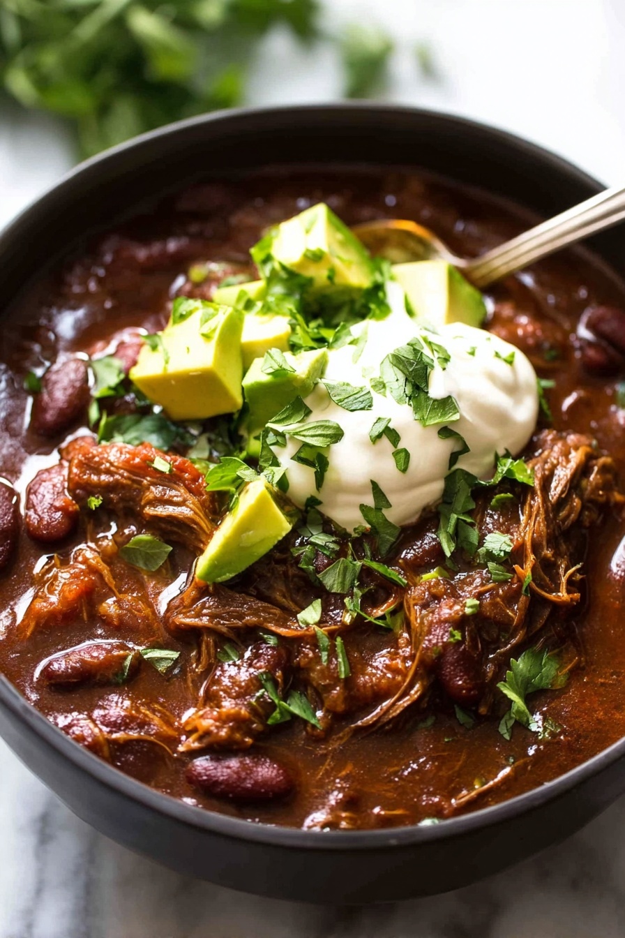 A close-up view of a black bowl filled with rich, chunky beef chili showing different textures. The first layer is a thick, dark reddish-brown chili base with beans and shredded meat visible. On top of this is a layer of melted yellow cheese that is slightly soft and stringy. Above the cheese sits a dollop of white sour cream, smooth and creamy in texture. Garnished on the sour cream are small cubes of light green avocado and a sprinkle of fresh green cilantro leaves. A silver spoon is placed inside the bowl on the right side, slightly submerged in the chili. The background features a white marbled surface with a blurred hint of greenery. photo taken with an iphone --ar 2:3 --v 7